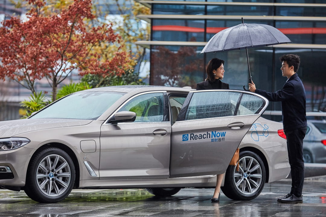 A ReachNow driver holding an umbrella for a customer